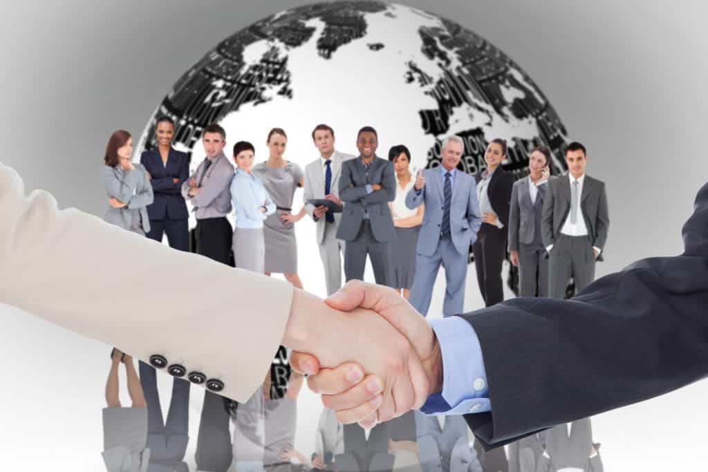 Smiling business people shaking hands while looking at the camera against white earth with business terms